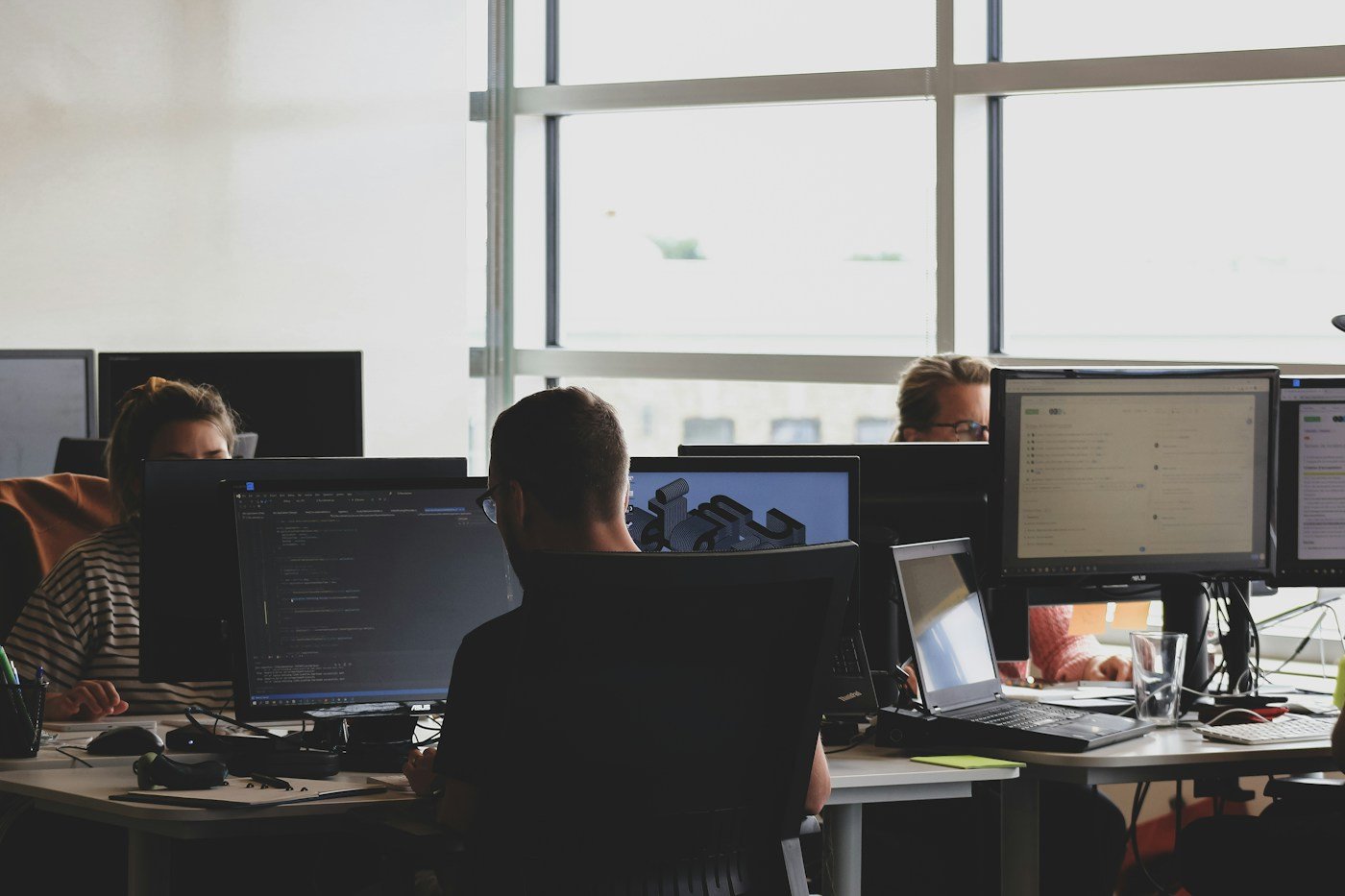 Colleagues working at neighbouring office desks with computer screens